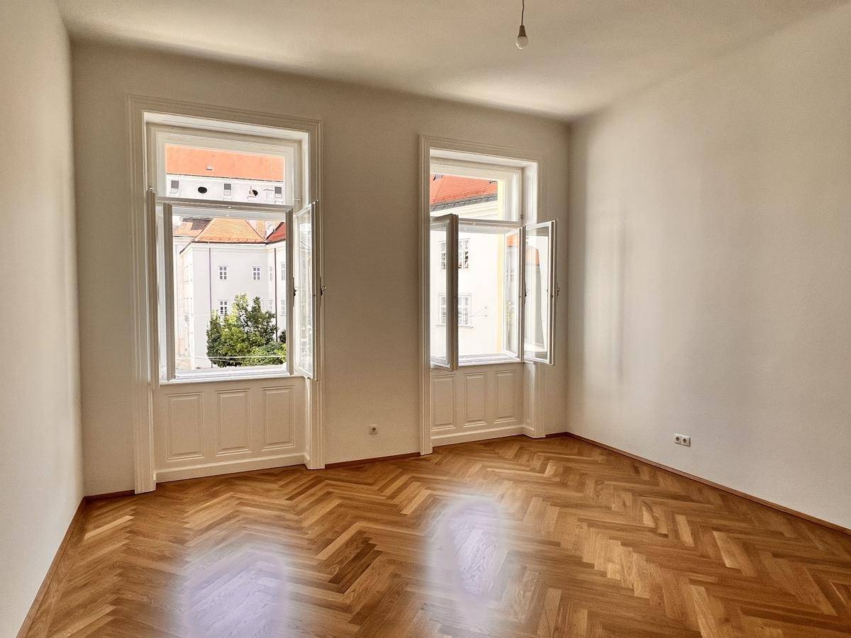 Heller Raum mit Fischgrätparkett und geöffneten Fenstern, die eine frische Atmosphäre schaffen.