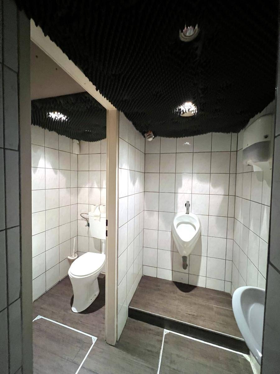 Öffentliche Toilettenanlage mit gefliesten Wänden, einem Urinal und einer Toilette in separaten Kabinen.