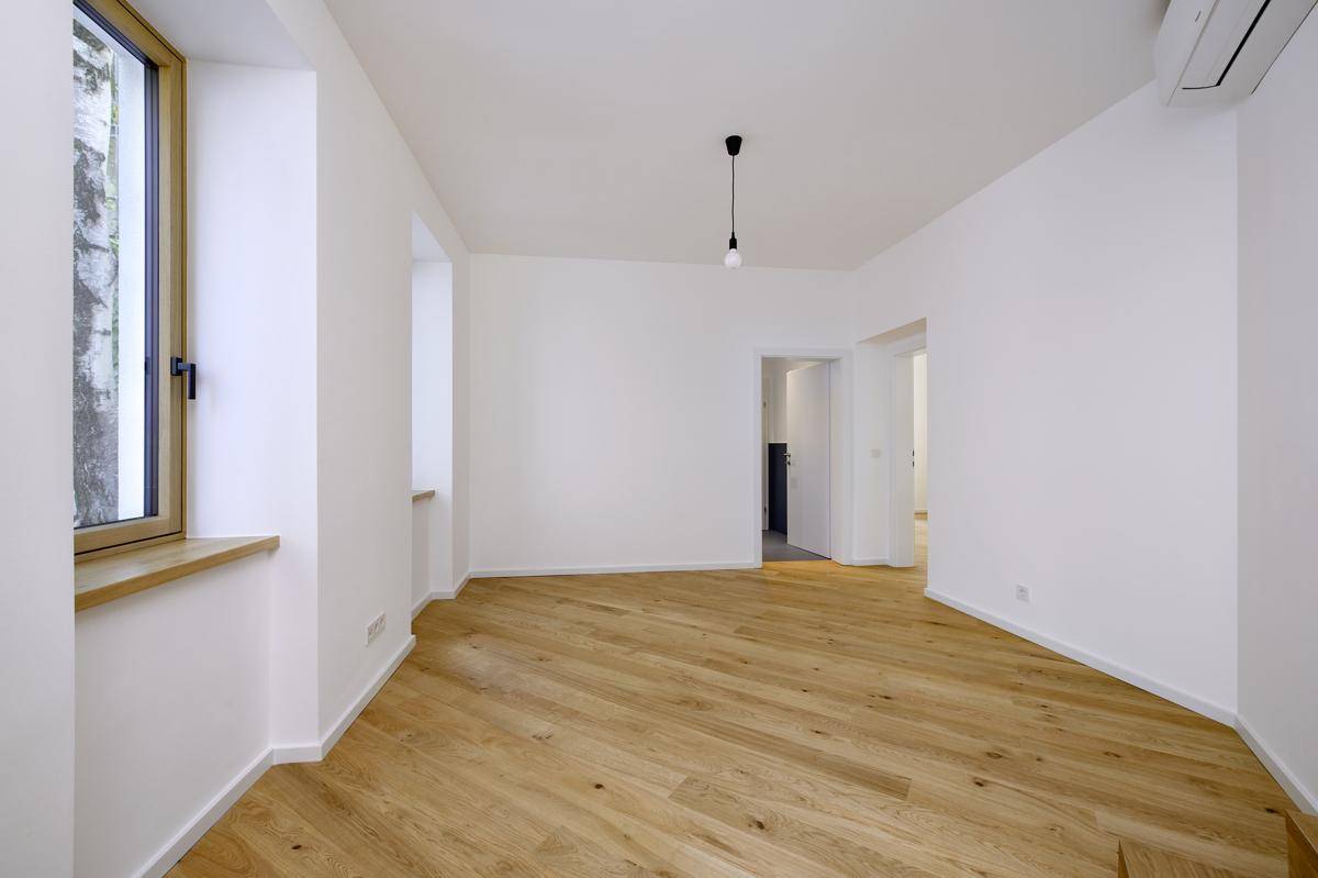 Ein heller Wohnraum mit Holzboden, großen Fenstern und einer Klimaanlage an der Wand.