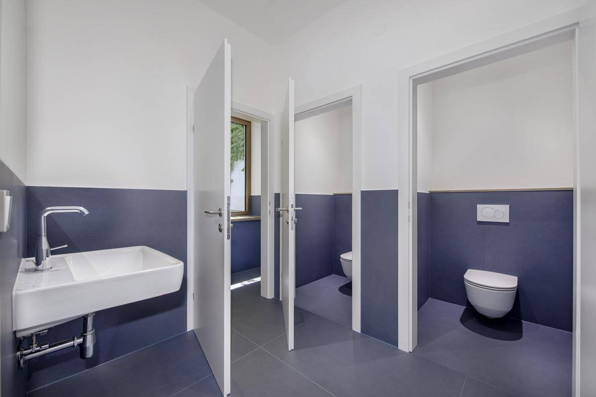 Mehrere Toilettenkabinen in einem modernen Sanitärbereich mit blauen Wandfliesen und Fenster.