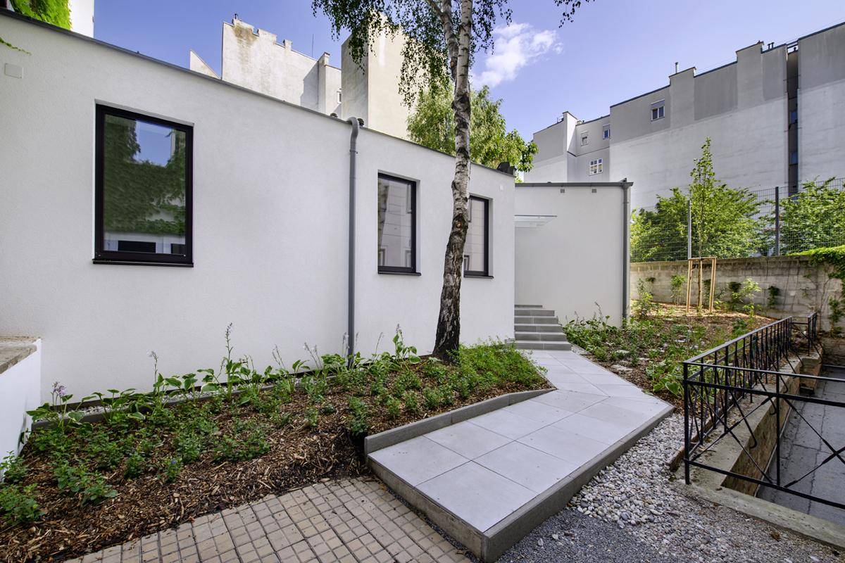 Eine moderne Gebäudefassade mit Fenstern und einem gepflegten Gartenbereich im Vordergrund.