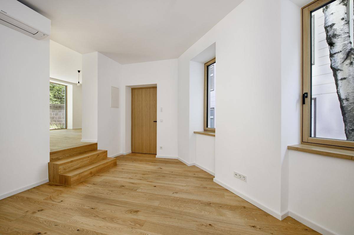 Ein heller Flur mit Holzboden, Holztreppe und Fenstern, die viel Tageslicht hereinlassen.