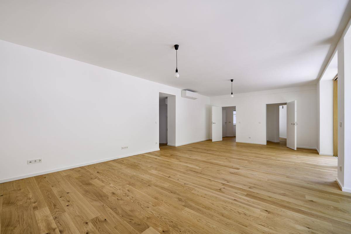 Ein heller, leerer Wohnraum mit Holzboden und mehreren Türen, bereit zur individuellen Gestaltung.
