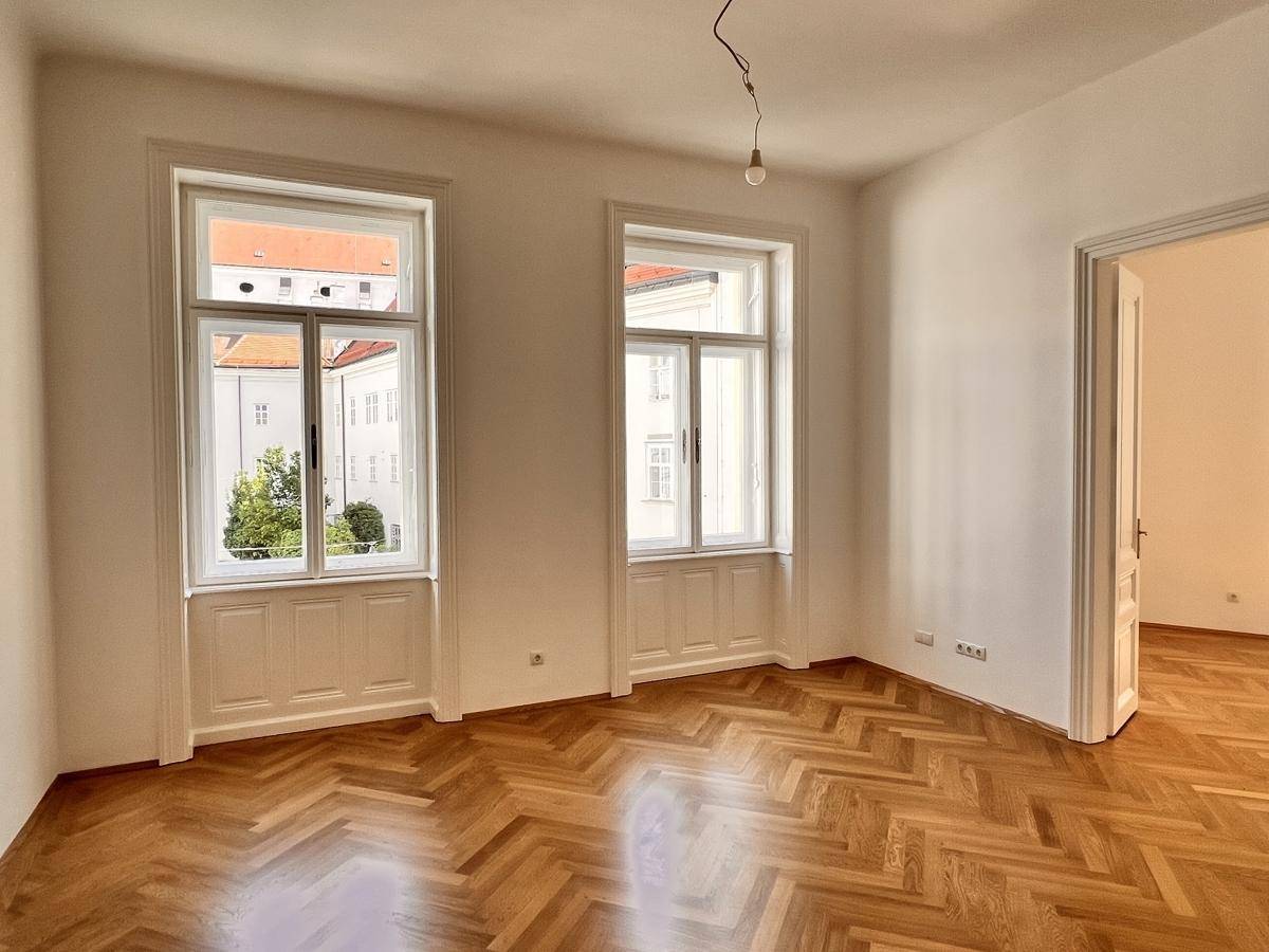 Heller Raum mit elegantem Fischgrätparkett und hohen Fenstern, die viel Tageslicht hereinlassen.