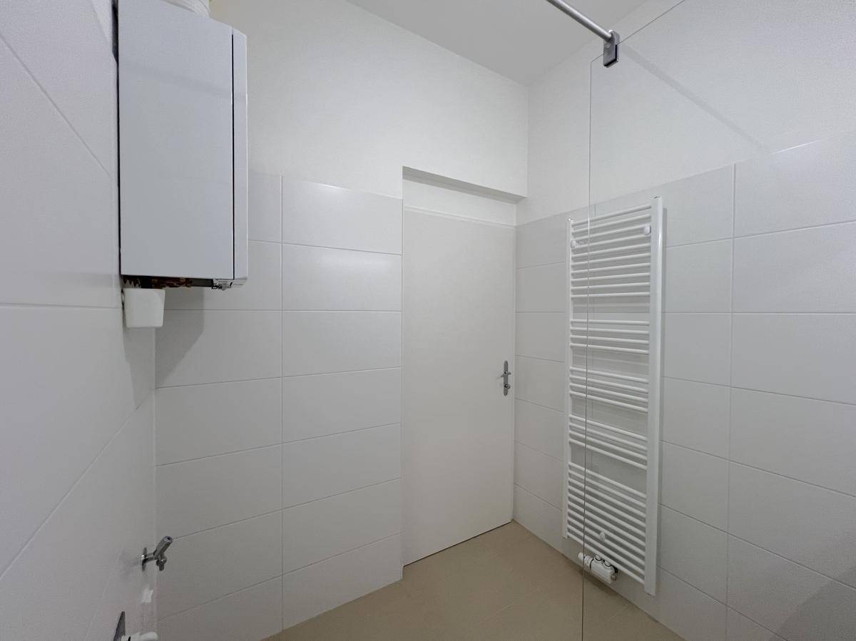 Funktionales Badezimmer mit weißen Fliesen, Handtuchheizkörper und Warmwasserbereiter.