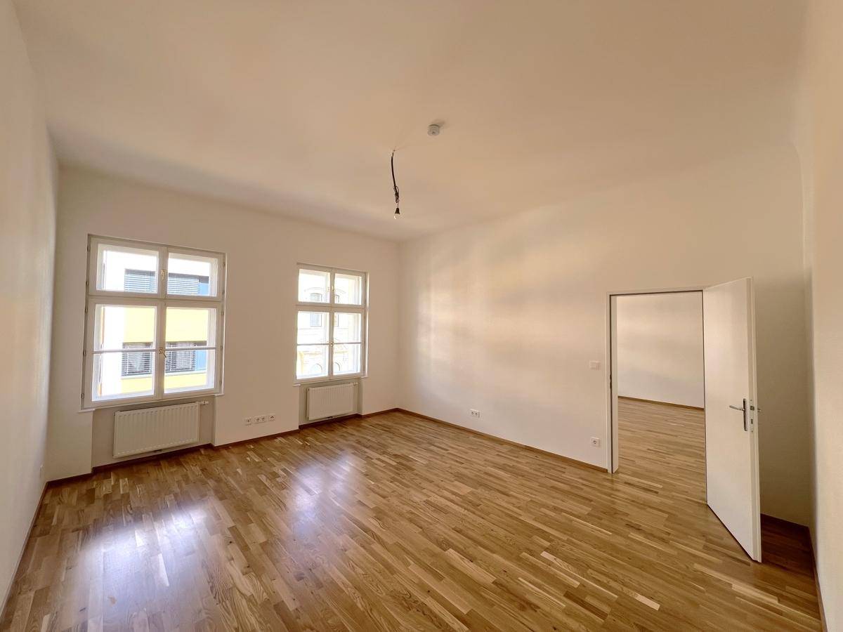 Geräumiges Zimmer mit hellem Parkettboden und großen Fenstern, ideal für Wohn- oder Schlafbereich.