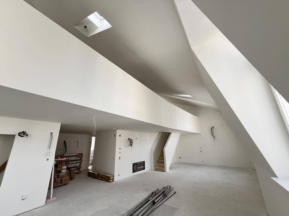 Offener Dachbodenbereich mit hohen Decken, Oberlichtern und sichtbaren Installationsvorbereitungen.