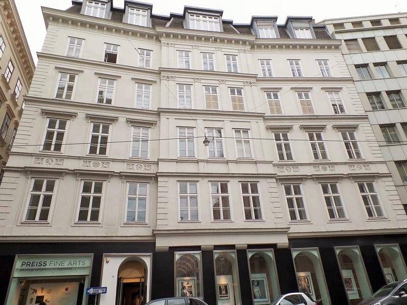 Klassische Fassade eines Mehrfamilienhauses mit vielen Fenstern und Geschäften im Erdgeschoss.