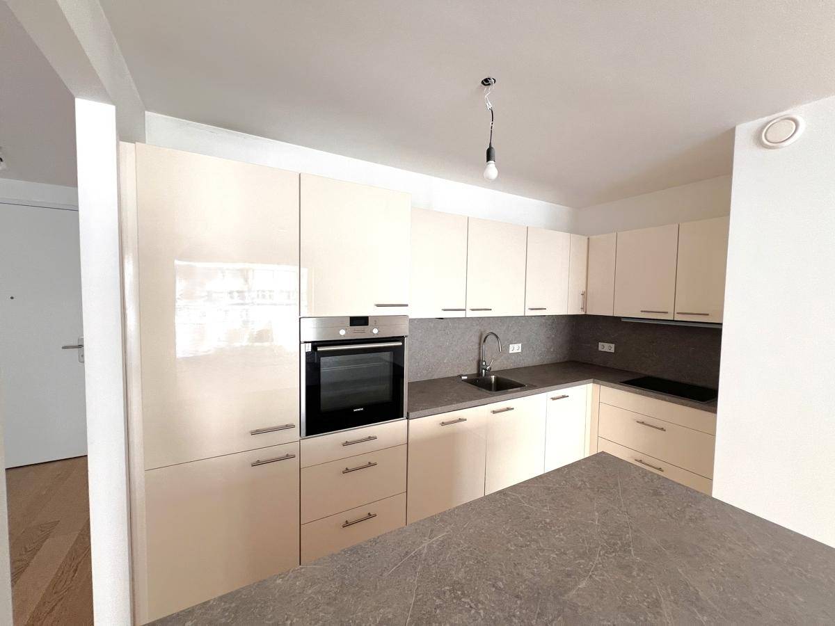 Moderne Einbauküche mit beigen Hochglanzschränken, integriertem Backofen und Kochfeld.