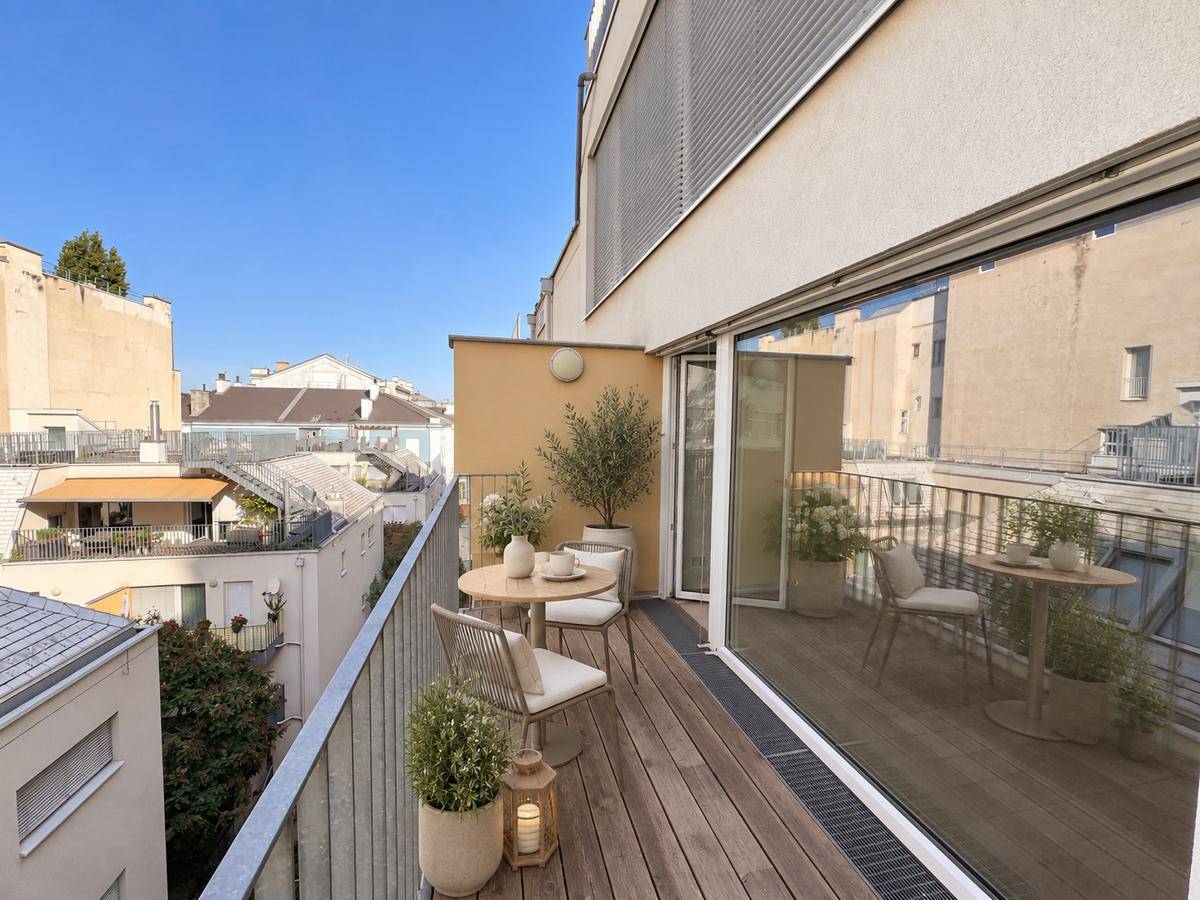 Möblierter Balkon mit Holzboden, Pflanzen und Blick auf die umliegenden Gebäude.