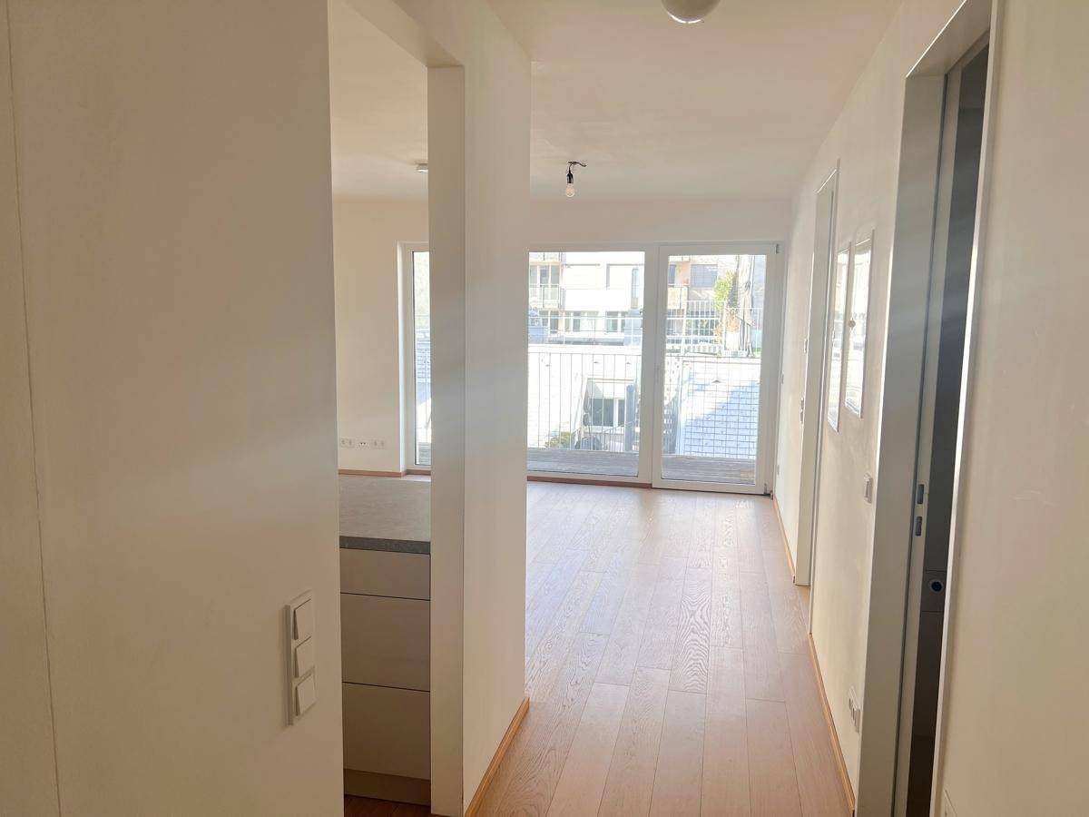 Heller Flur mit Holzboden, weißen Wänden und Zugang zu weiteren Räumen und Balkon.