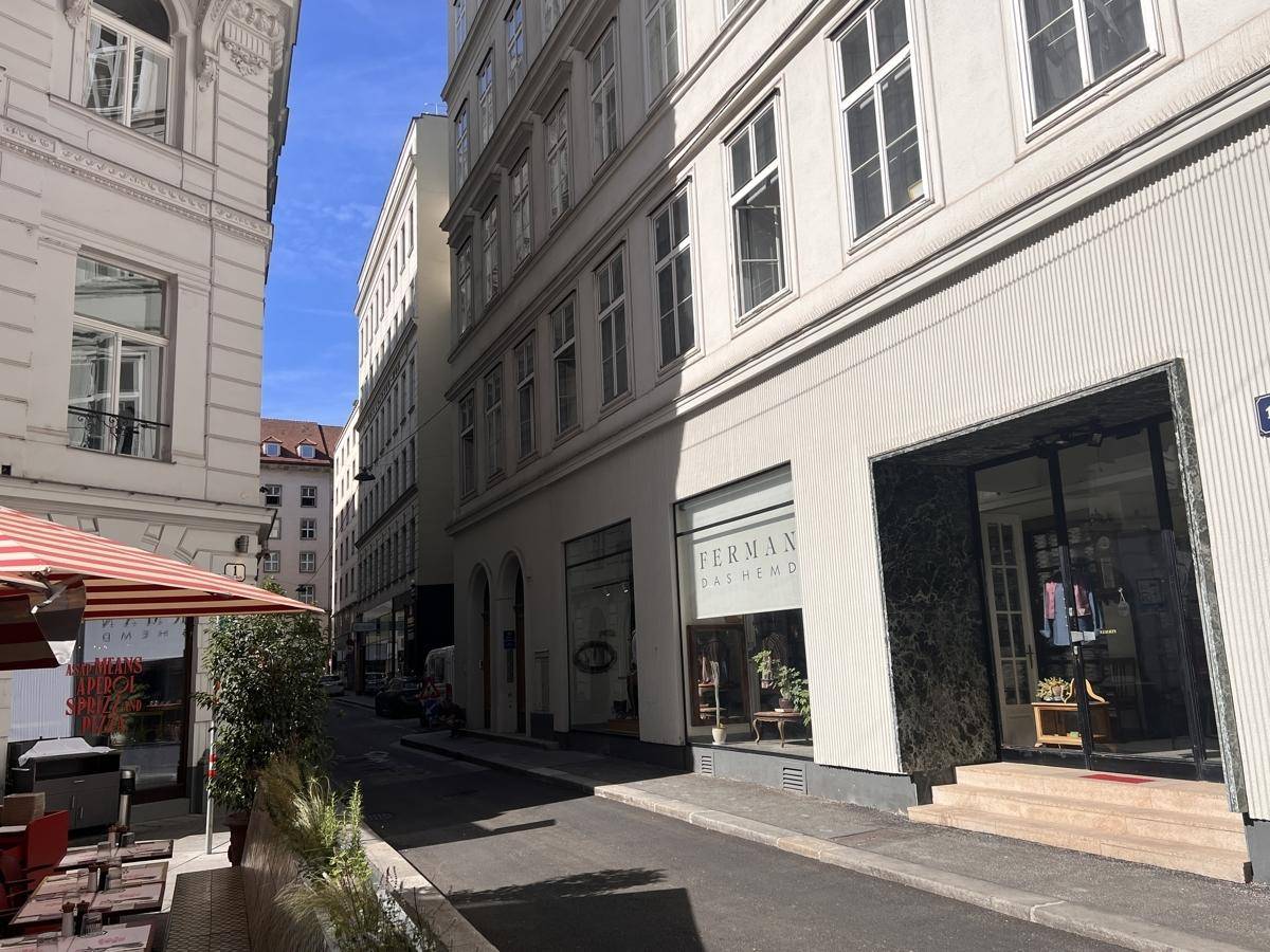 Historische Straßenansicht mit eleganten Gebäudefassaden und Geschäften im Erdgeschoss.