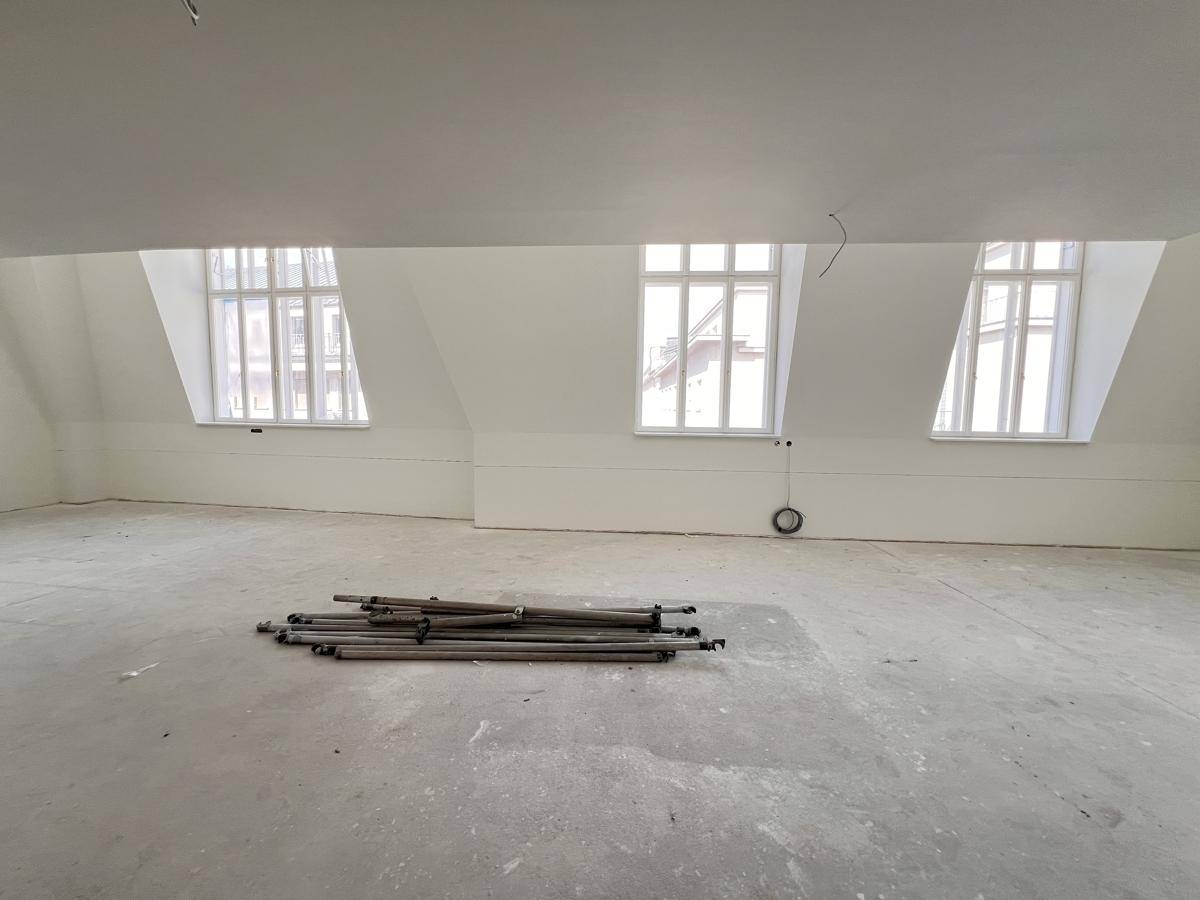 Großer, unmöblierter Dachbodenraum mit drei Fenstern und schrägen Wänden, ideal für Ausbau.