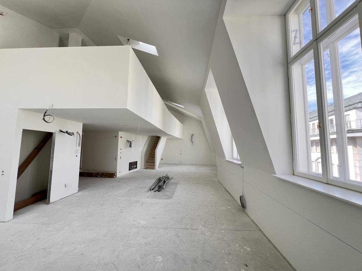 Offener Dachbodenbereich mit hohen Decken, großen Fenstern und sichtbaren Installationsvorbereitungen.