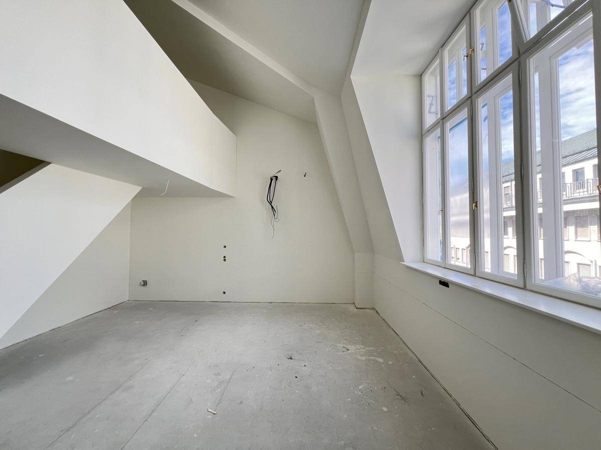 Heller, unmöblierter Dachbodenraum mit großen Fenstern und schrägen Wänden, bereit für den Ausbau.
