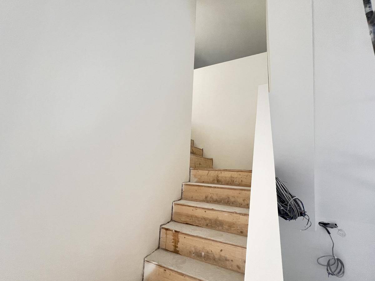 Unfertige Holztreppe in einem Rohbau mit weißen Wänden und sichtbaren Kabeln.