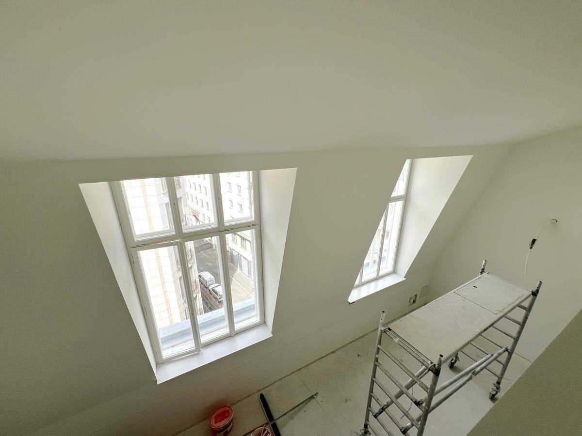 Heller Dachgeschossraum mit großen Fenstern und einem Baugerüst, das auf den bevorstehenden Ausbau hinweist.