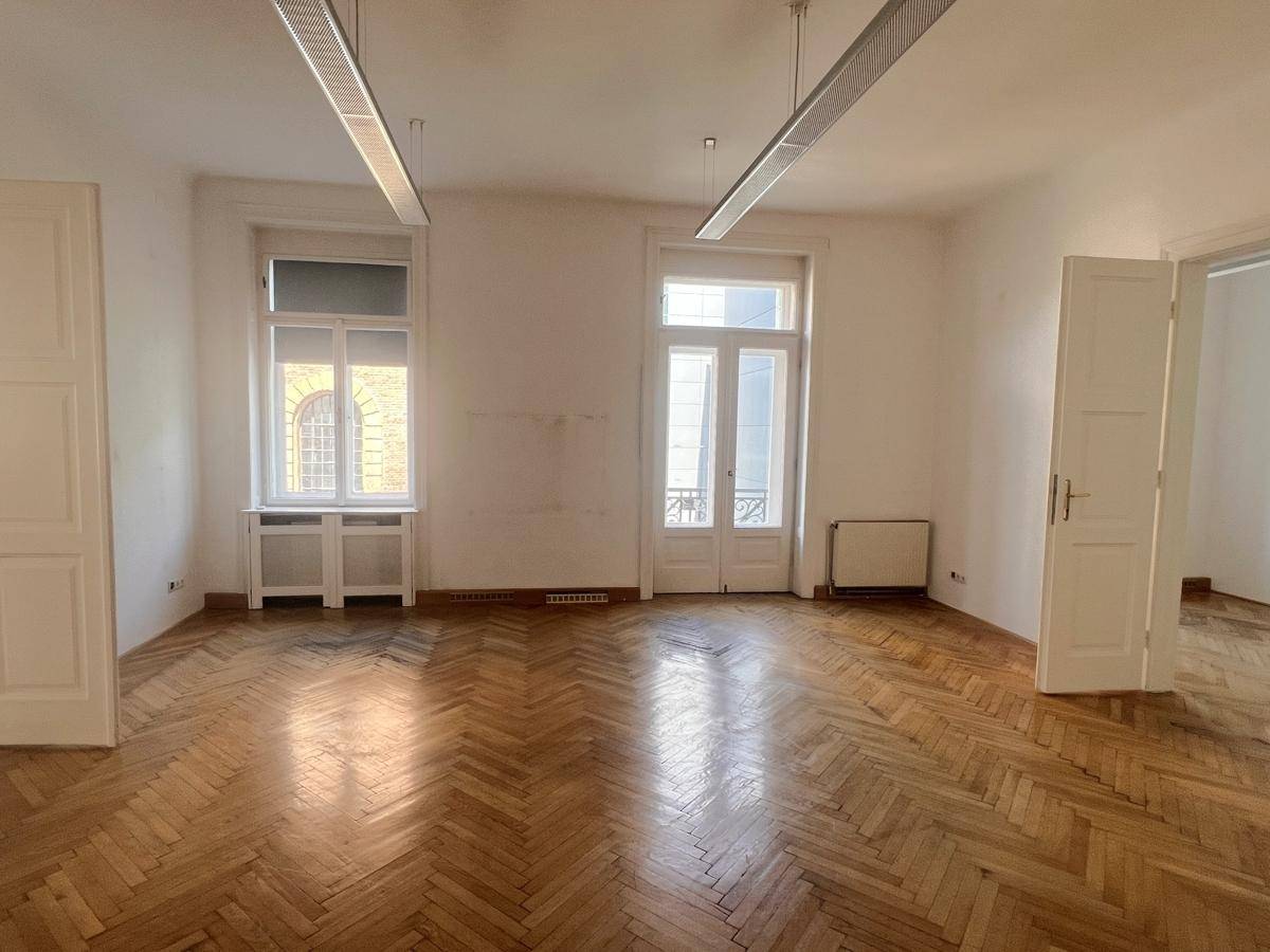 Leeres Büro mit klassischem Fischgrätparkett und hohen Fenstern, die viel Tageslicht hereinlassen.