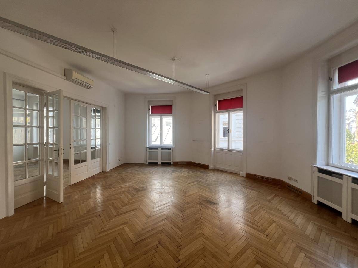 Helles Büro mit Fischgrätparkett, Klimaanlage und großen Fenstern mit roten Rollos.