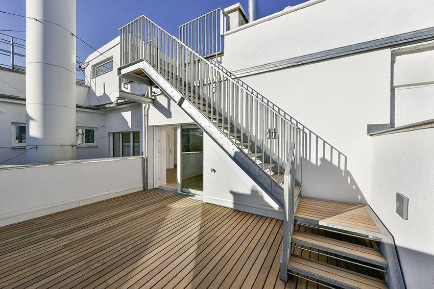 Dachterrasse mit Holzbelag und Außentreppe, die zu einer weiteren Ebene führt.