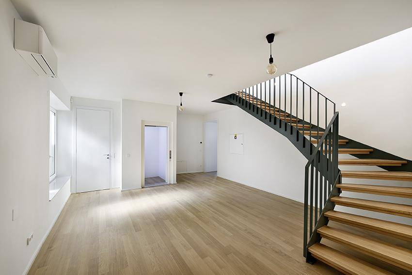 Heller Eingangsbereich mit moderner Treppe, Aufzug und Parkettboden.