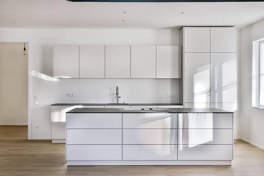 Moderne Einbauküche mit weißen Hochglanzfronten, dunkler Arbeitsplatte und viel Stauraum.