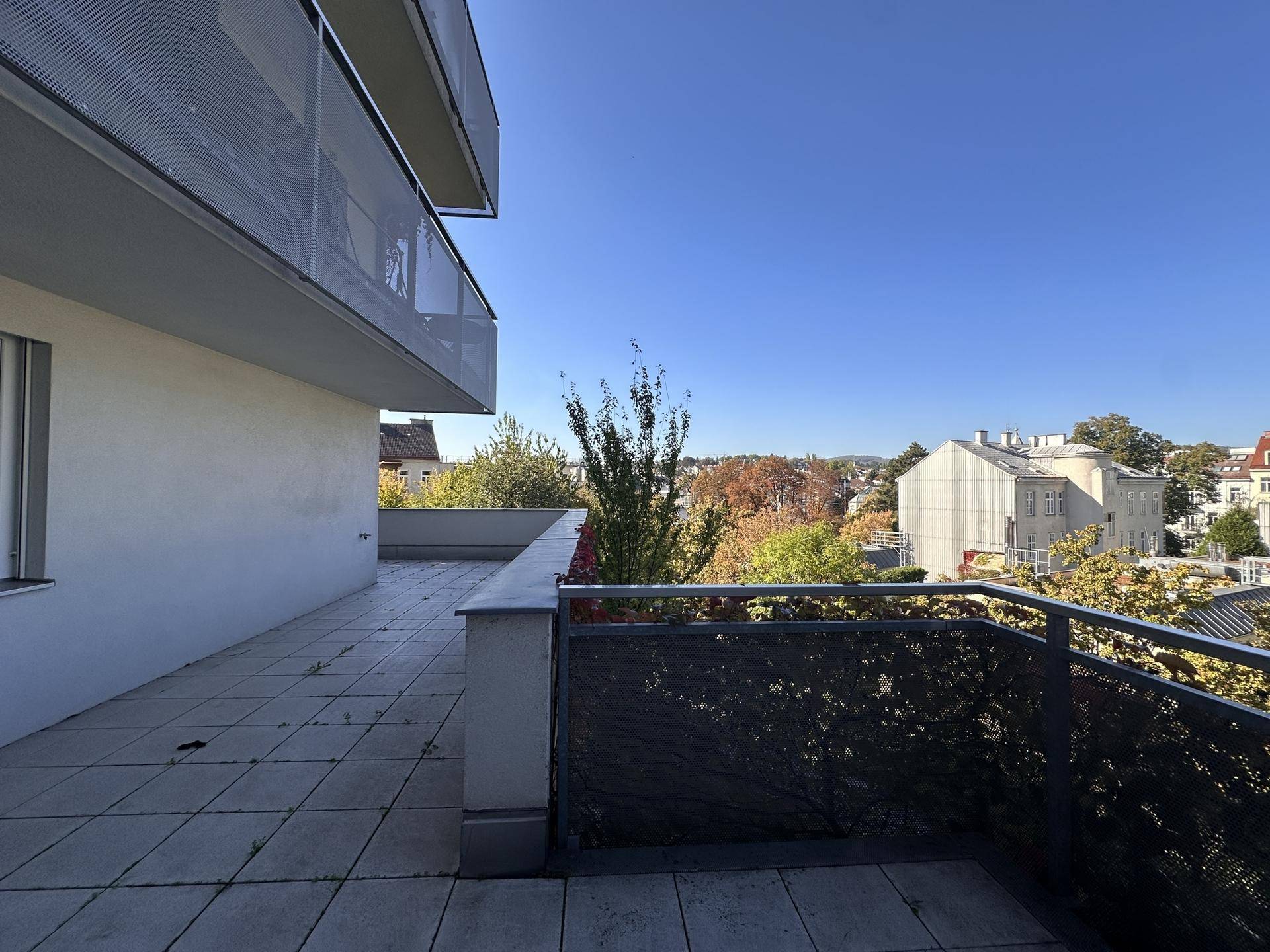 Balkon mit Metallgeländer und weitem Blick über die grüne Umgebung und Dächer.