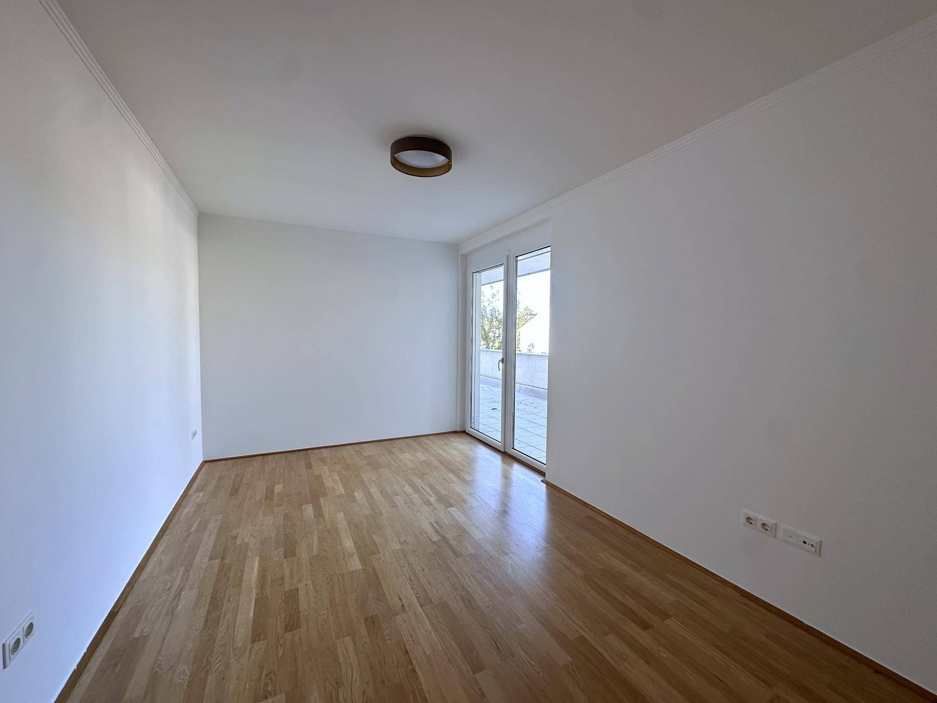 Leeres Zimmer mit Holzboden und Zugang zu einem Balkon, bereit zur individuellen Gestaltung.