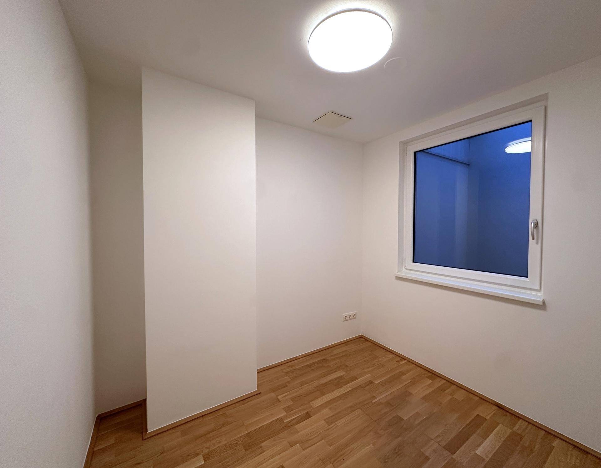 Leeres Zimmer mit Holzboden und Fenster, ideal als Büro oder Gästezimmer nutzbar.