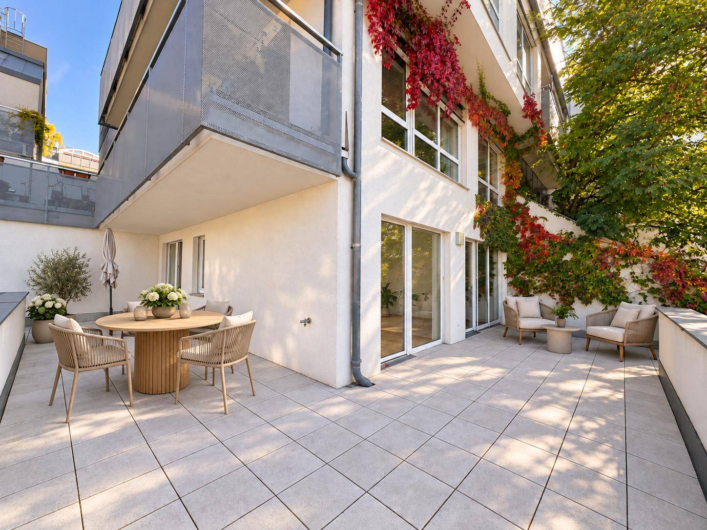 Großzügige Terrasse mit Sitzbereich, Fliesenboden und begrünten Wänden am Gebäude.