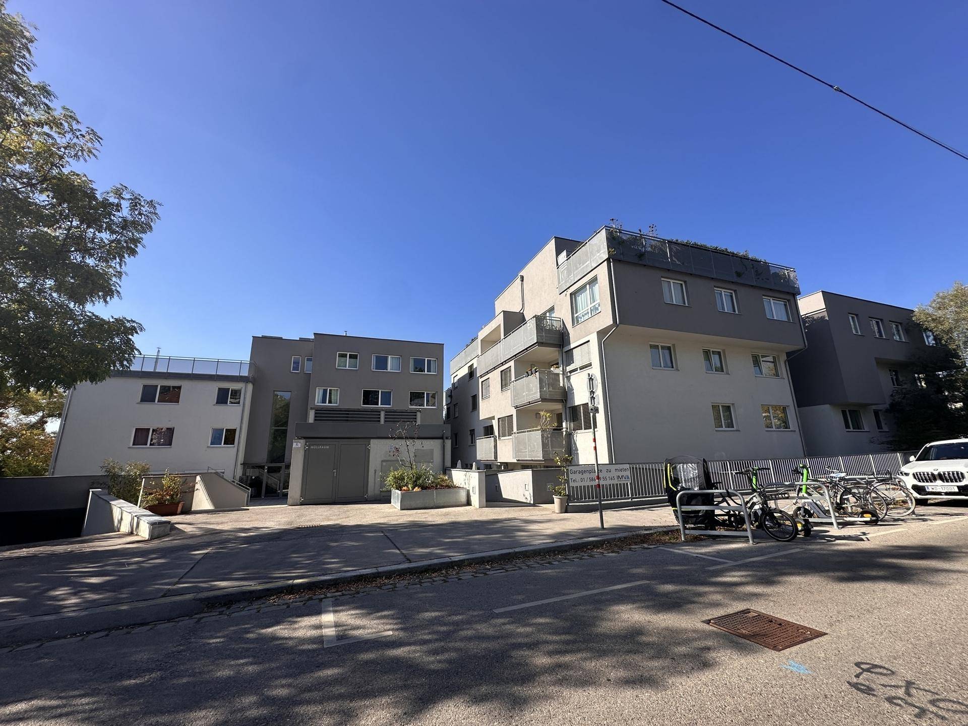 Moderne Wohnanlage mit mehreren Gebäuden, Balkonen und Parkmöglichkeiten an der Straße.