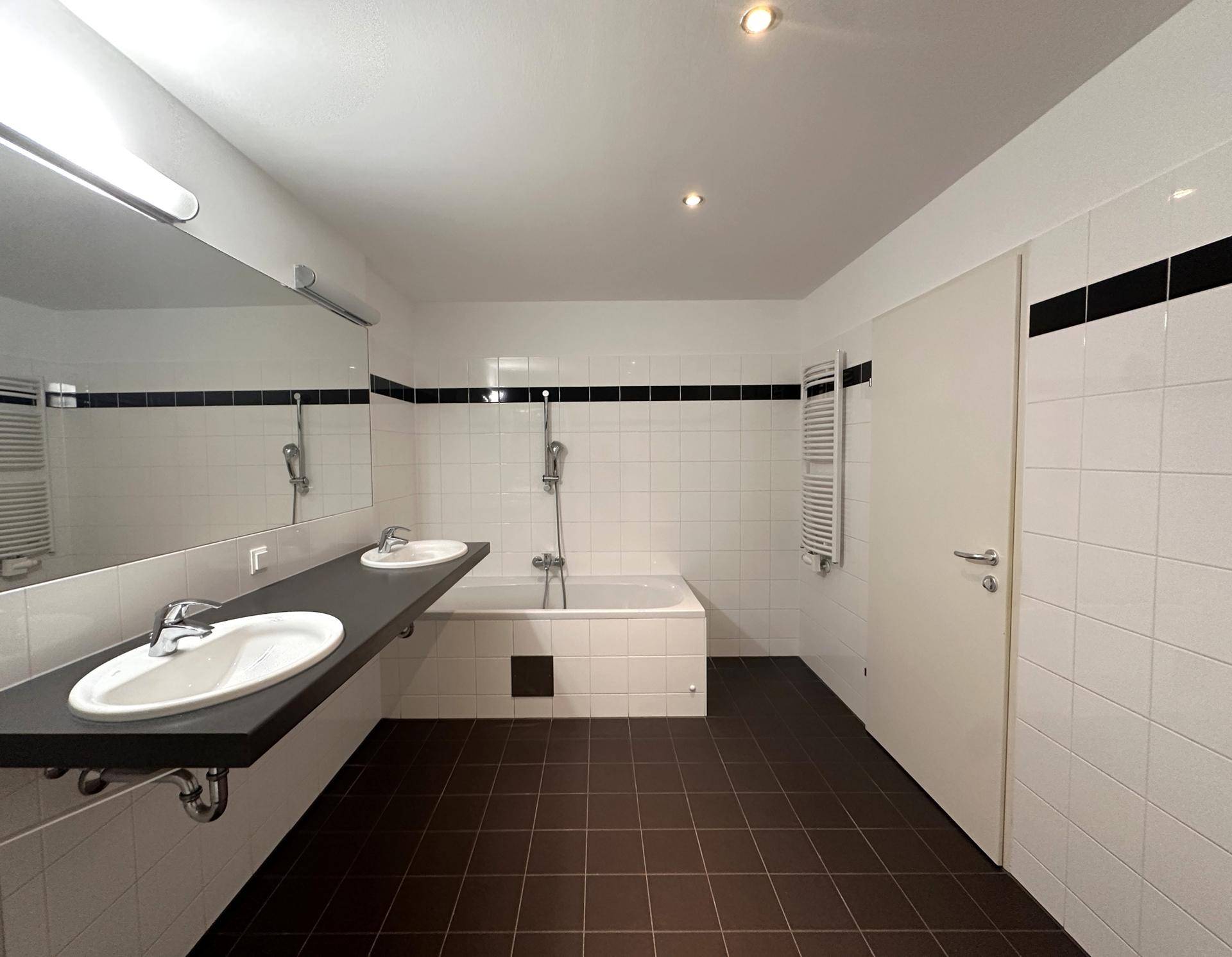 Geräumiges Badezimmer mit Badewanne, Doppelwaschbecken und beheiztem Handtuchhalter.