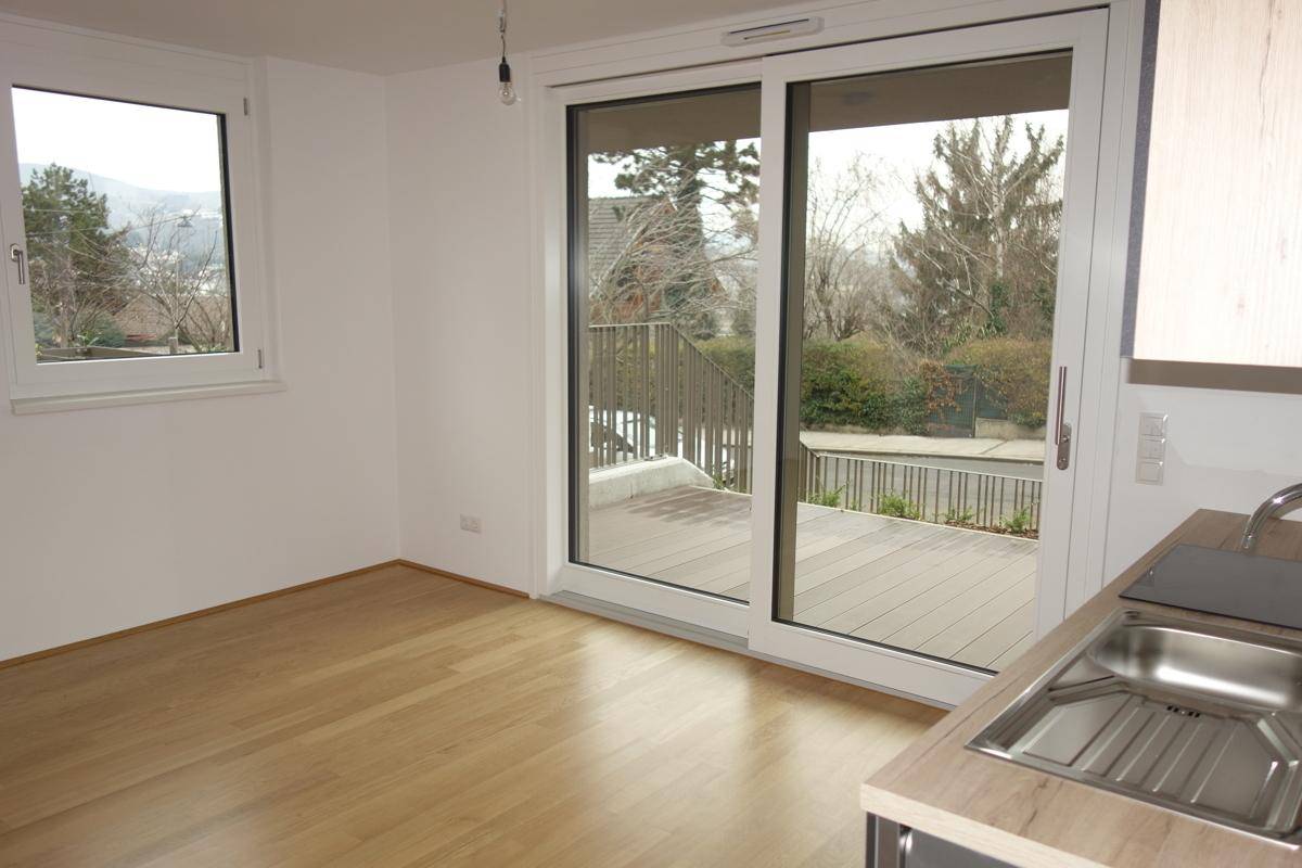 Heller Wohnbereich mit Parkettboden und großem Fenster mit Zugang zu einer Terrasse.