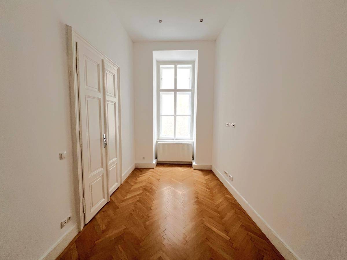 Schmaler Raum mit Fischgrätparkett, einem Fenster und einer eleganten Doppeltür.