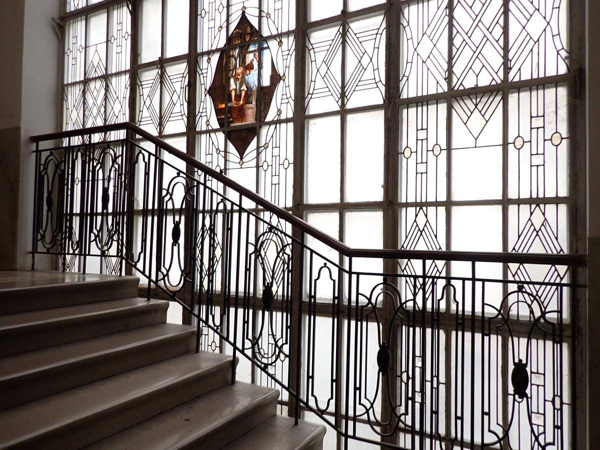 Elegantes Treppenhaus mit kunstvollem Metallgeländer und großen Fenstern mit dekorativer Bleiverglasung.