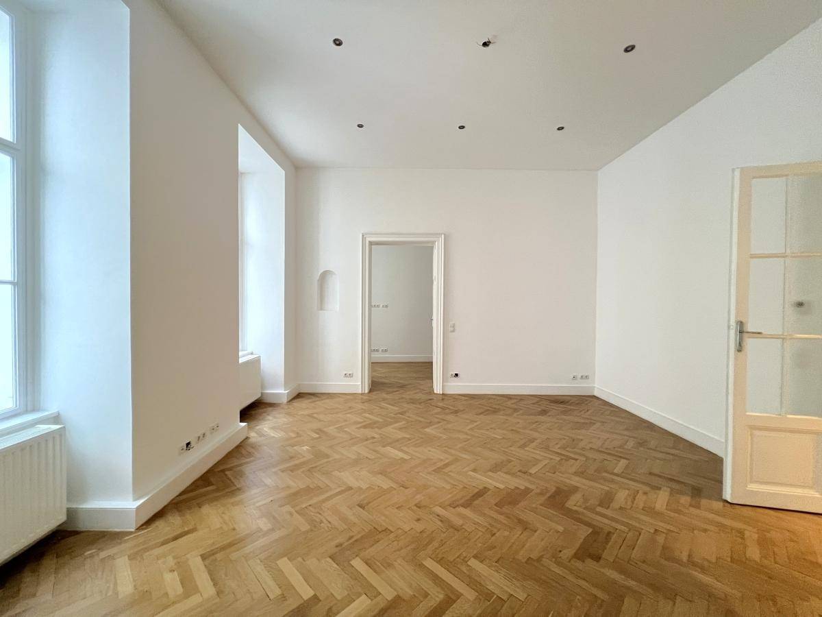 Heller Raum mit elegantem Fischgrätparkett und einem Durchgang zu weiteren Zimmern.
