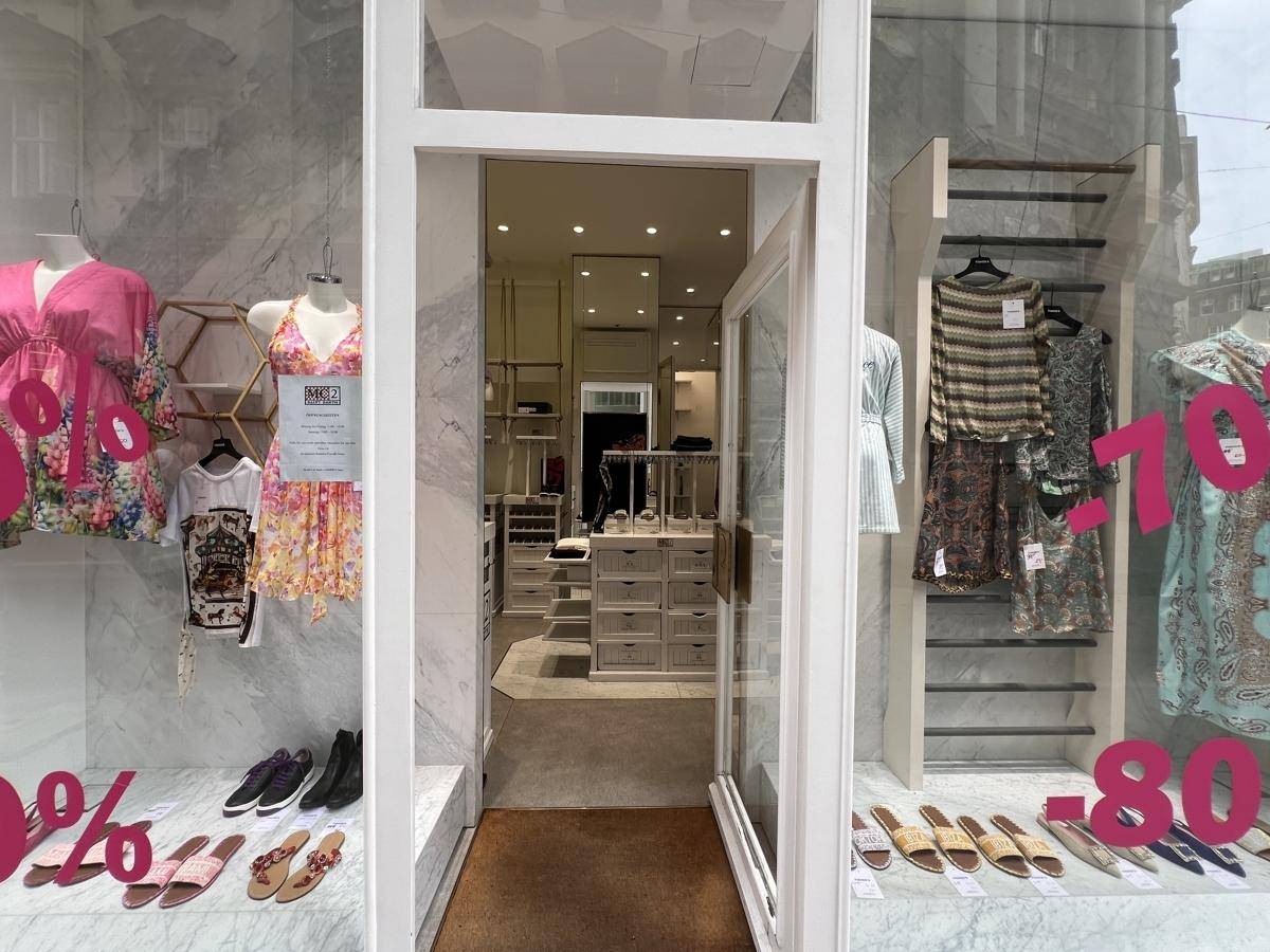 Eingangsbereich eines Bekleidungsgeschäfts mit Schaufenster, das Kleidung und Rabattschilder zeigt.