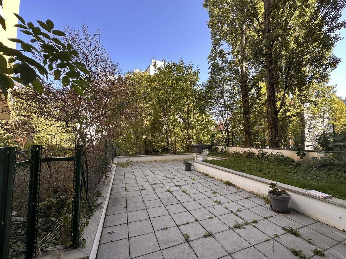 Große geflieste Terrasse mit Grünflächen und Bäumen, ideal für Entspannung im Freien.