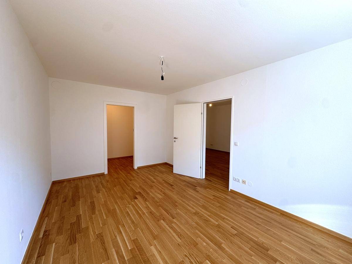 Heller, leerer Raum mit Parkettboden und Zugang zu weiteren Zimmern.