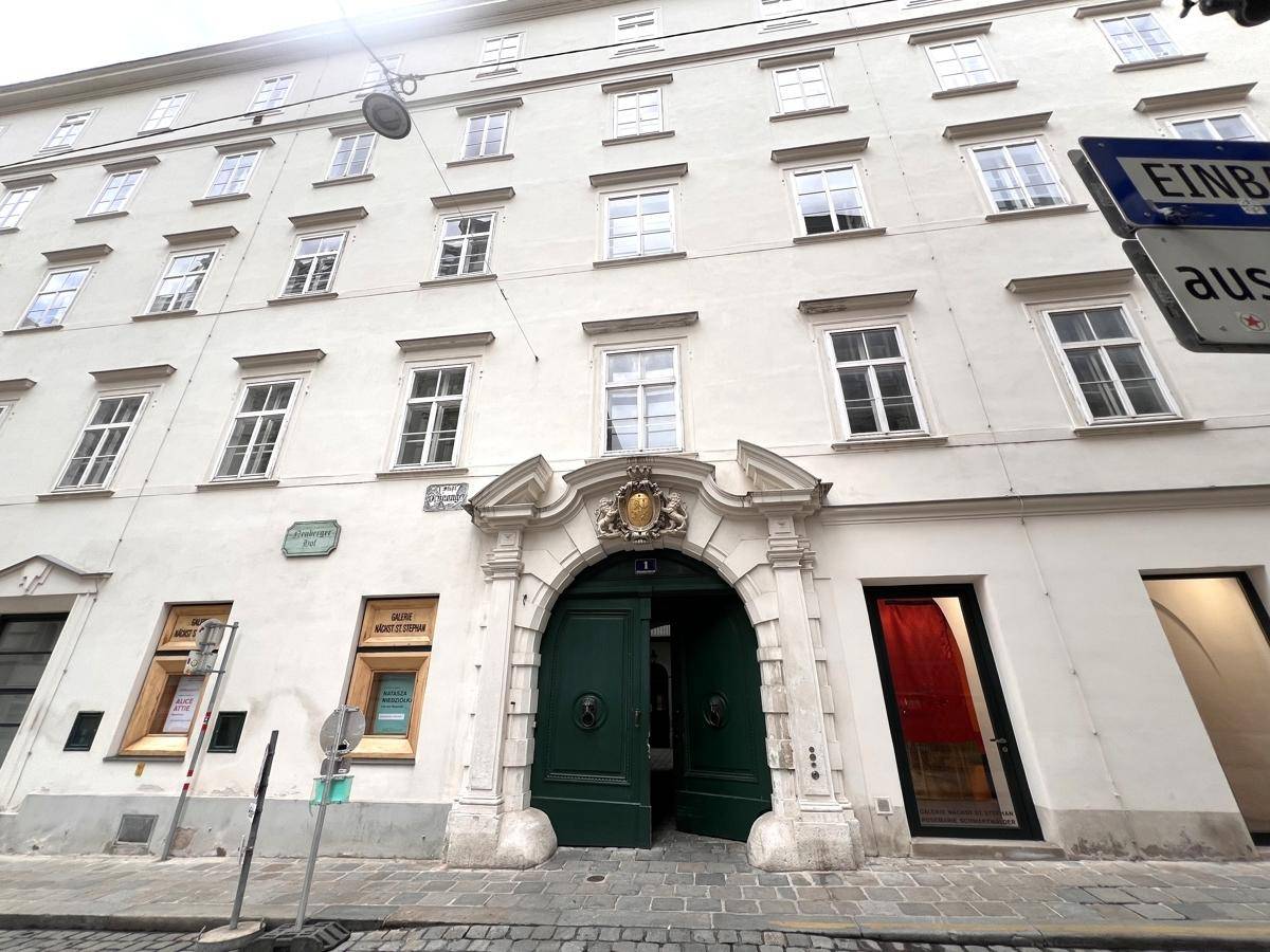Historische Fassade eines Gebäudes in der Stadt mit gepflasterter Straße und parkenden Autos.
