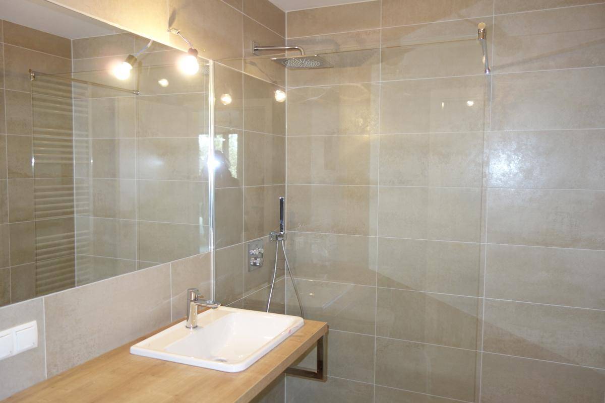 Modernes Badezimmer mit beigefarbenen Fliesen, Einzelwaschbecken und Regendusche.