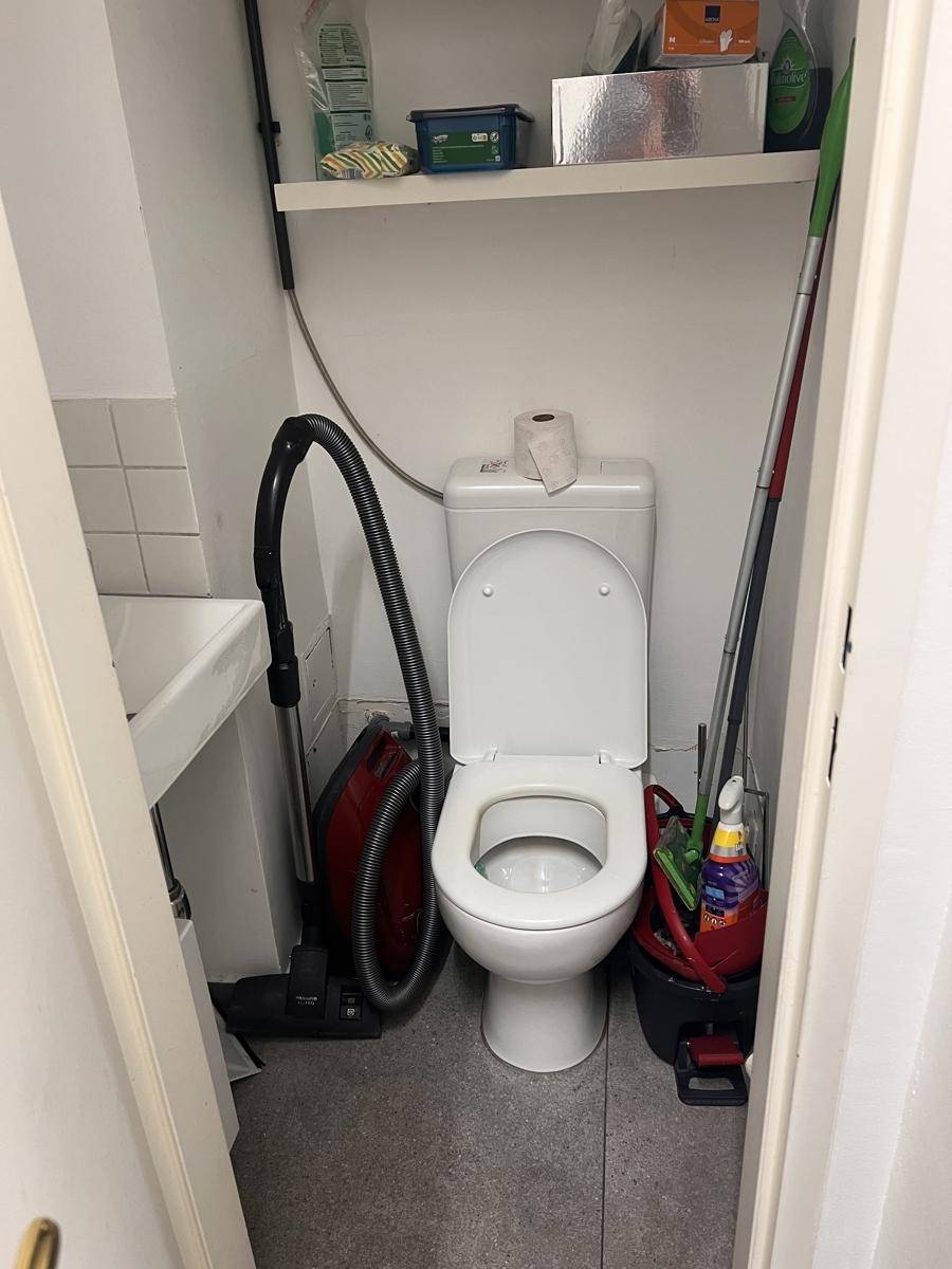 Kleiner Toilettenraum, der auch als Abstellraum für Reinigungsgeräte und einen Staubsauger genutzt wird.