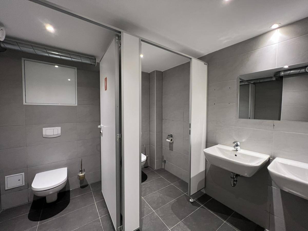 Moderne, geflieste Toilettenanlage mit mehreren Kabinen, Waschbecken und Spiegel, in gutem Zustand.