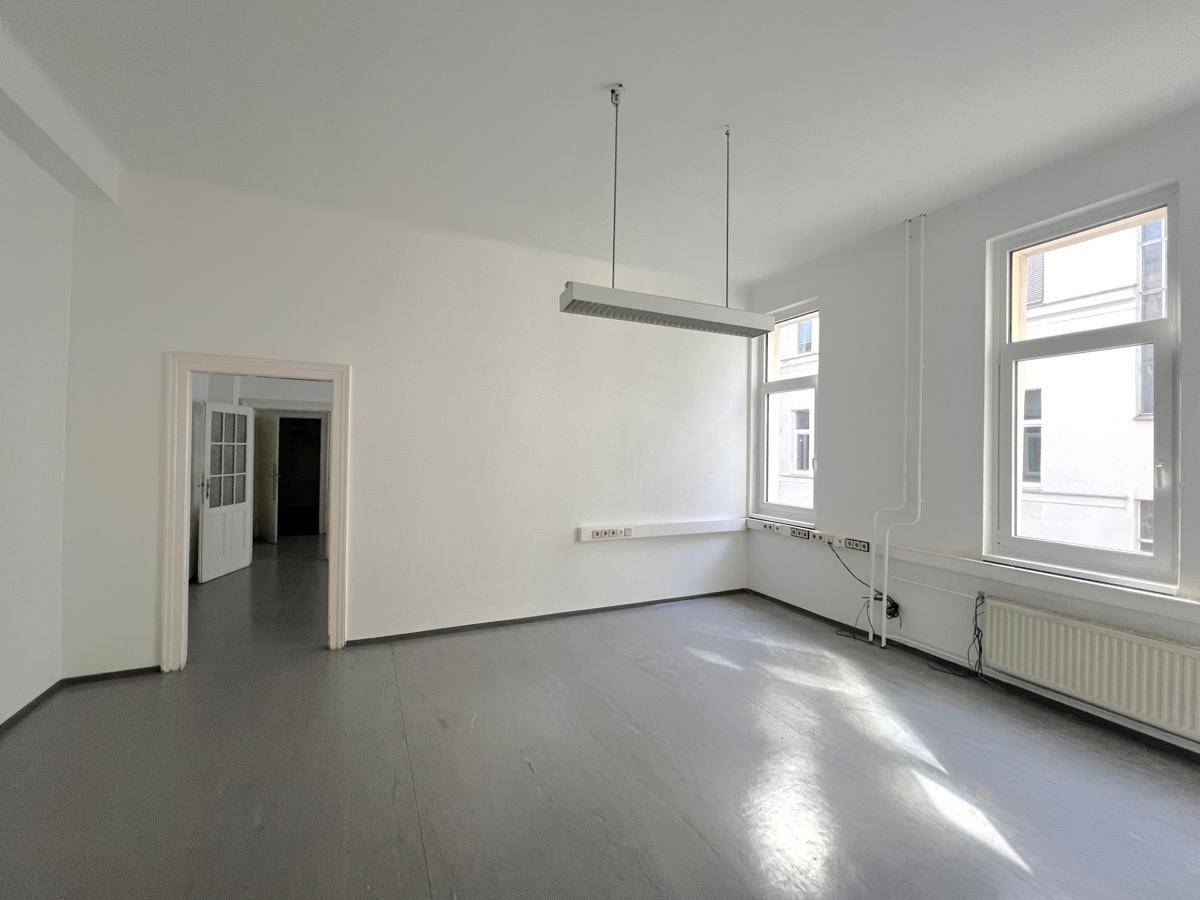 Geräumiges Büro mit grauem Boden, weißen Wänden und großen Fenstern, die eine angenehme Arbeitsatmosphäre schaffen.