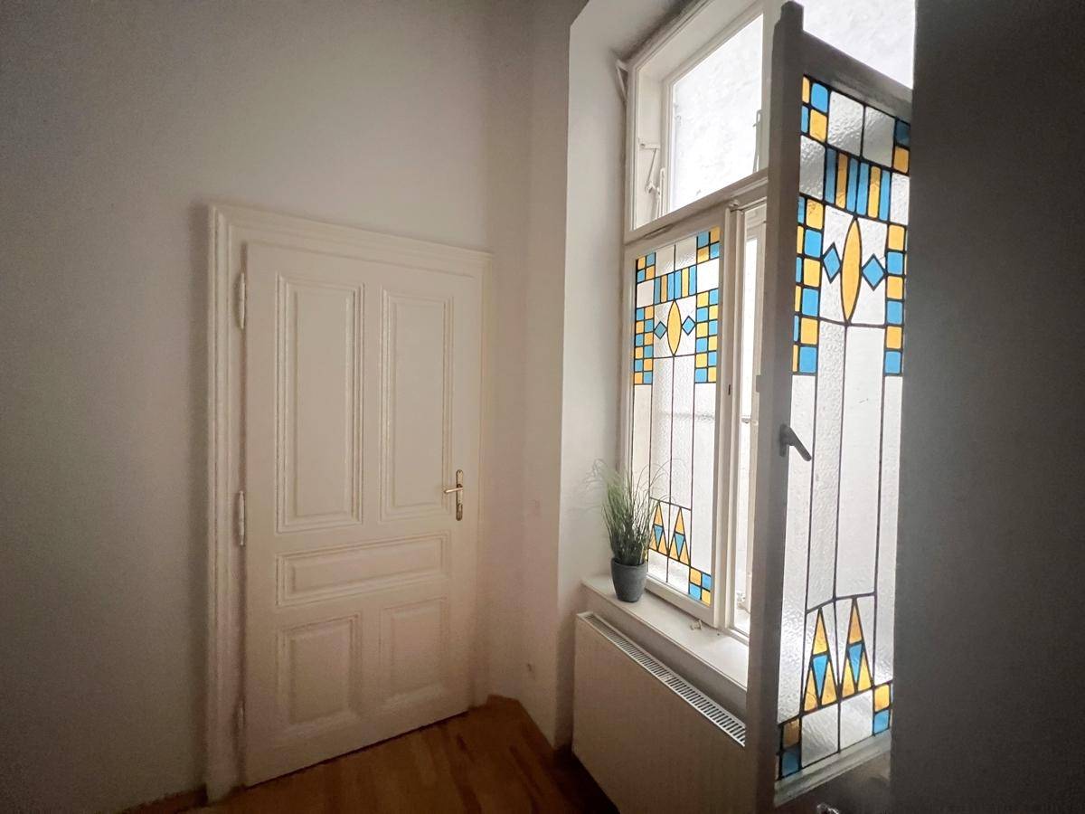 Flur mit einer Tür und einem farbenfrohen Buntglasfenster, das natürliches Licht hereinlässt.
