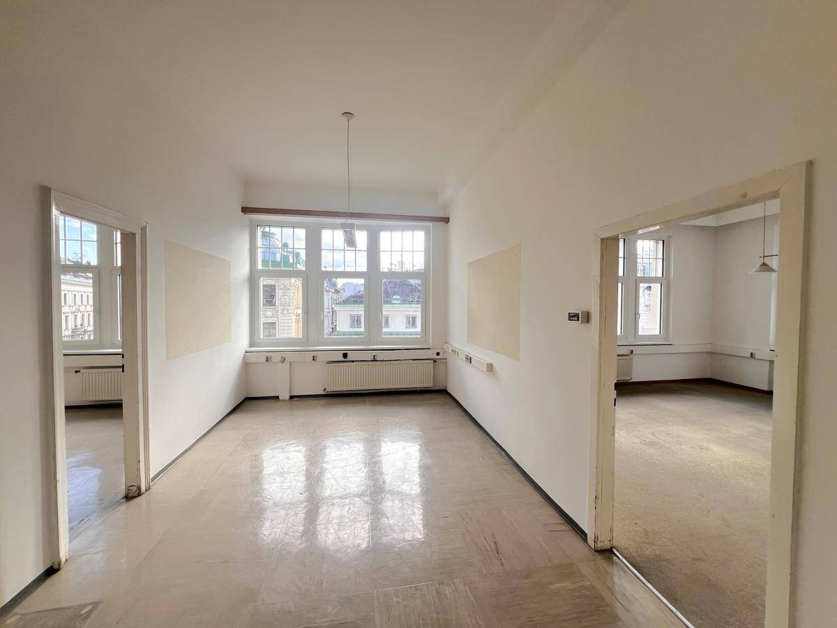 Geräumiges Büro mit hellem Boden, vielen Fenstern und Zugang zu weiteren Räumen, ideal für Bürogemeinschaften.
