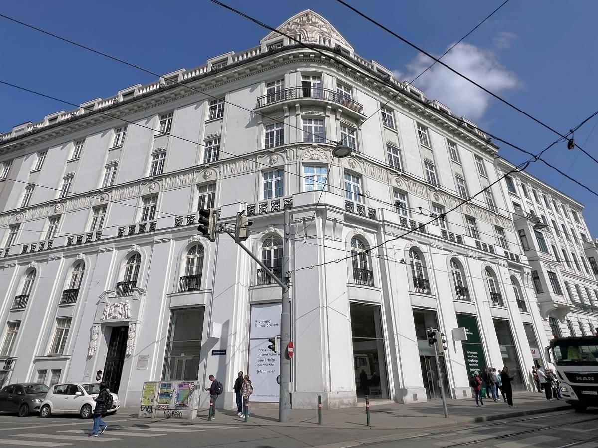 Elegantes Eckgebäude mit historischer Fassade und vielen Fenstern in einer städtischen Umgebung unter blauem Himmel.