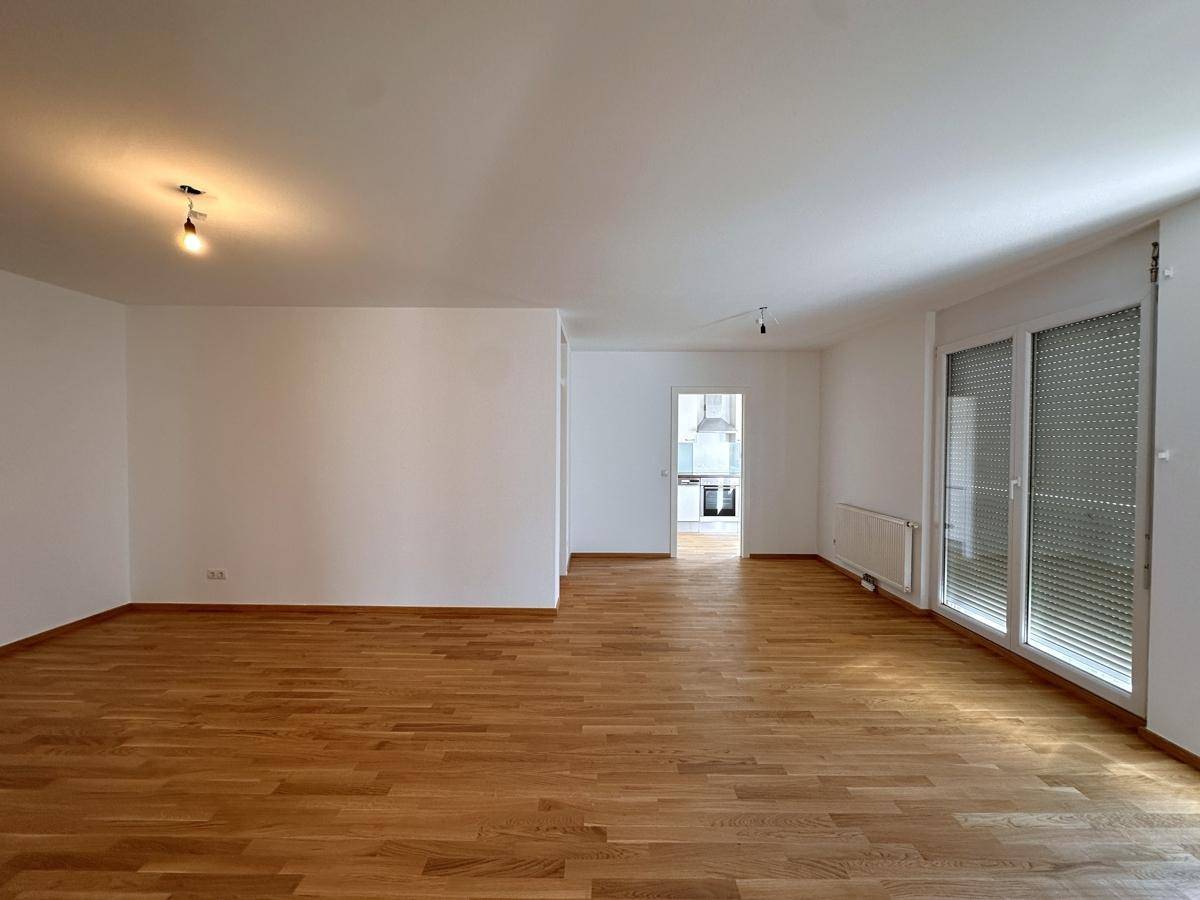 Geräumiger, leerer Wohn- und Essbereich mit hellem Parkettboden und großen Fenstern.