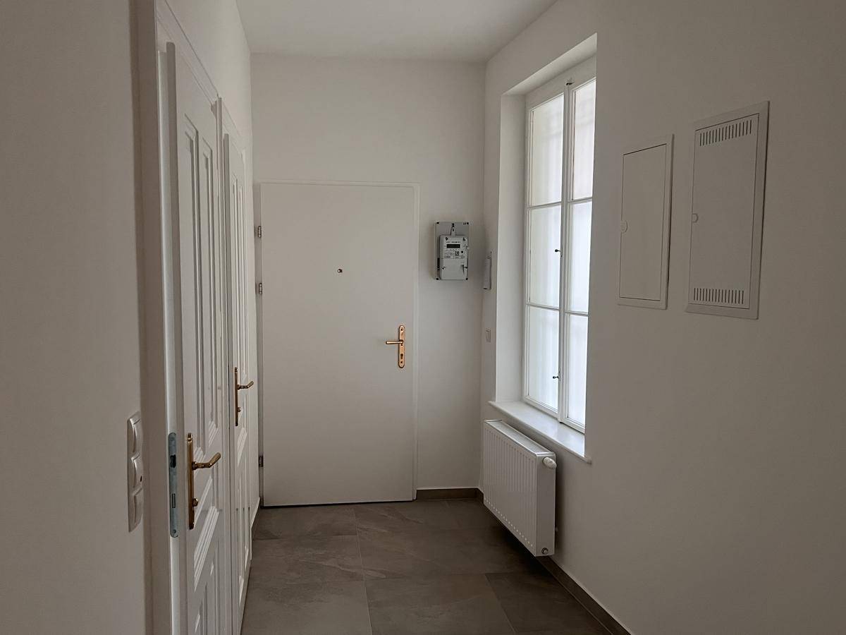 Heller Eingangsbereich mit Fliesenboden, Fenster und Heizkörper.