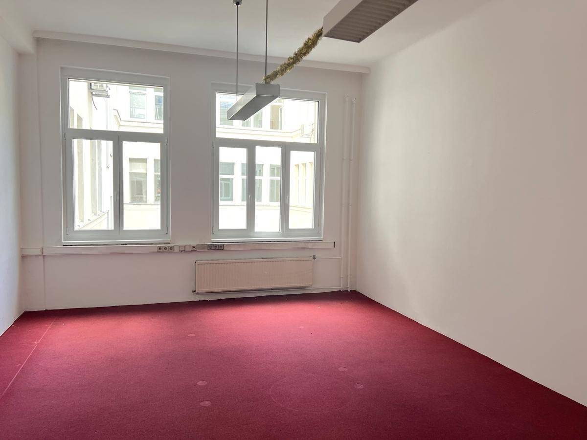 Leeres Büro mit auffälligem rotem Teppichboden, weißen Wänden und zwei großen Fenstern für Tageslicht.